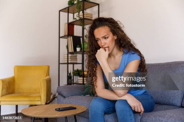 anxious young woman sitting on the sofa, biting her nails, contemplating - introspection stock pictures, royalty-free photos & images