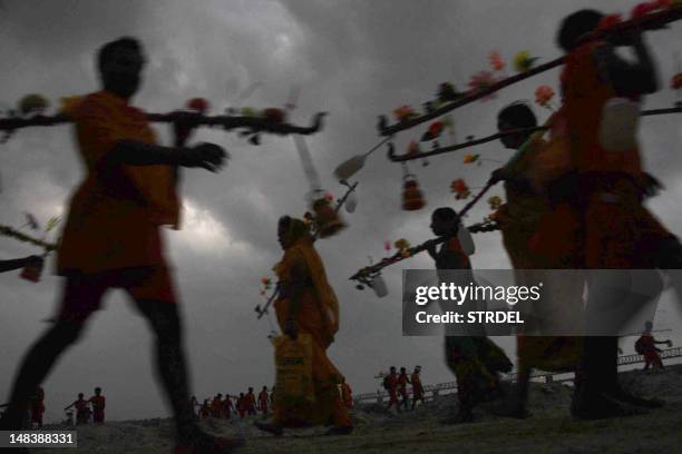 Hindu pilgrims or Kanwarias carry ornately decorated pots of sacred water as they walk on the banks of the holy river Ganga during the Hindu lunar...