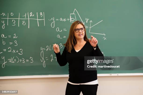 senior female math teacher writing on board in classroom. - blackboard qc stock pictures, royalty-free photos & images