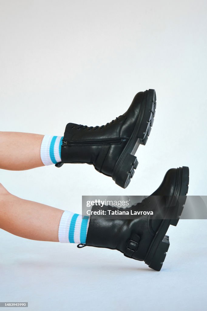 Beautiful female legs in long white socks and rough black boots. Conceptual image of shoes with copy space