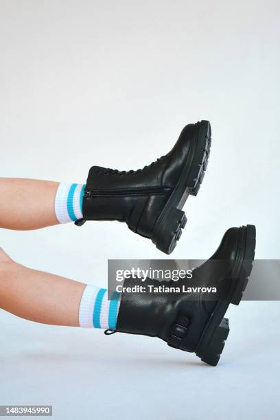 beautiful female legs in long white socks and rough black boots. conceptual image of shoes with copy space - booties stock pictures, royalty-free photos & images