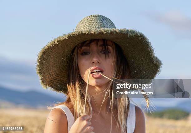 Frontal Closeup View Of A Beautiful Woman Standing In A Field Looking Sensually At The Camera Holding And Biting A Wheat, Stock-Foto
