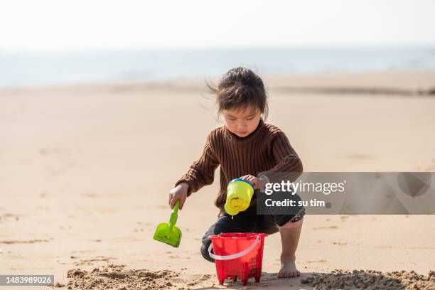 a girl makes plastic tools playing sand on the beach - beach bucket stock pictures, royalty-free photos & images