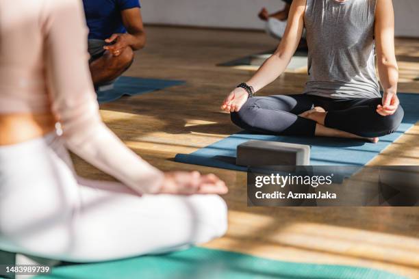 diverse yoga class participants sitting on yoga mats in a sukhasana pose during their yoga session - yoga class stock pictures, royalty-free photos & images