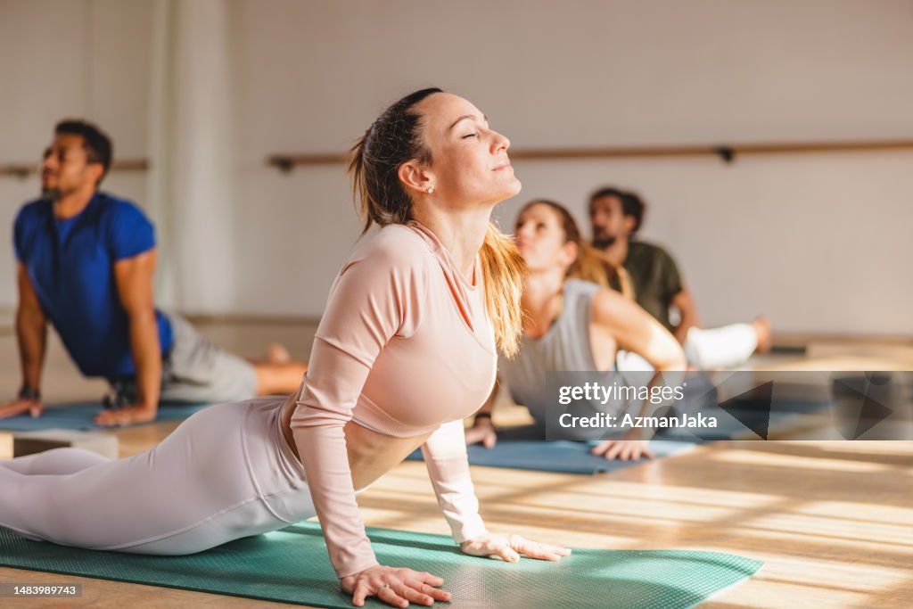 Eine attraktive Frau mit geschlossenen Augen, die während einer Yogastunde in einem schönen Studio mit natürlichem Sonnenlicht eine Kobra-Pose macht