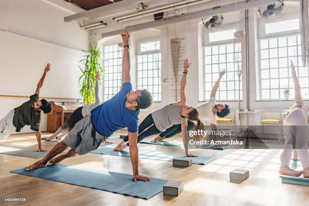 Verschiedene Yoga-Kursteilnehmer machen eine Seitenplanke auf ihren Yogamatten in einem wunderschönen Yoga-Studio mit großen Fenstern