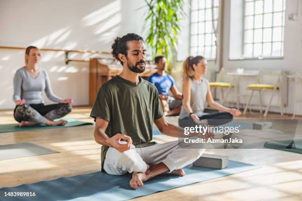 erwachsener arabischer mann mit einem pferdeschwanz, der in einer yogastunde meditiert - yoga stock-fotos und bilder