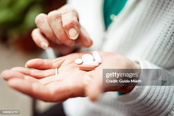 senior woman holding pills in hand - farmaci foto e immagini stock