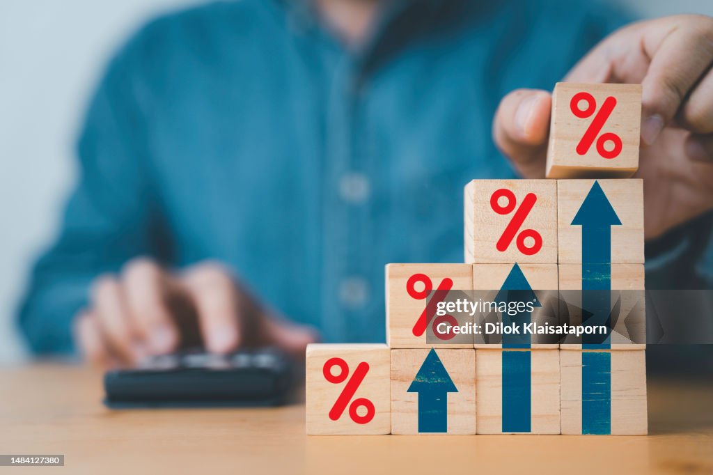 Geschäftsmann, der ein rotes Prozentzeichen mit steigendem Aufwärtspfeil für den Finanzzinssatz und das Wachstum der Unternehmensinvestitionen aus dem Dividendenkonzept setzt.