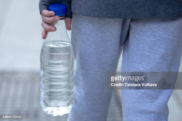 rear view photo of ubrecognizable teenage boy carrying a plastic bottle in hand filled with water while walking around the city - 背中 手 ストックフォトと画像