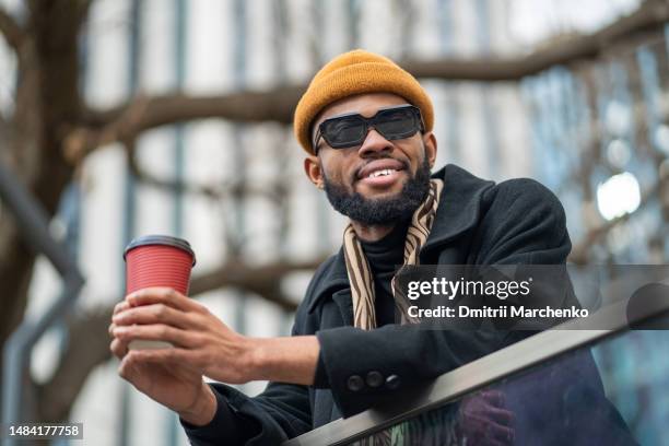 smiling happy black man in sunglasses looking side holding takeaway coffee think about success life - leisure work coffee happy stockfoto's en -beelden