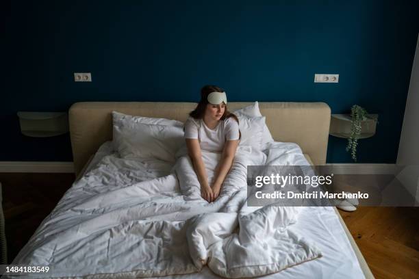 exhausted unhappy woman wearing sleep eye mask sitting in bed feeling tired depressed after wake up - negative emotion stock pictures, royalty-free photos & images