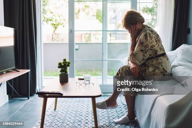 anxiety and memory loss. senior woman crying with face in hands against bright window in nursing home ward - memory loss stock-fotos und bilder