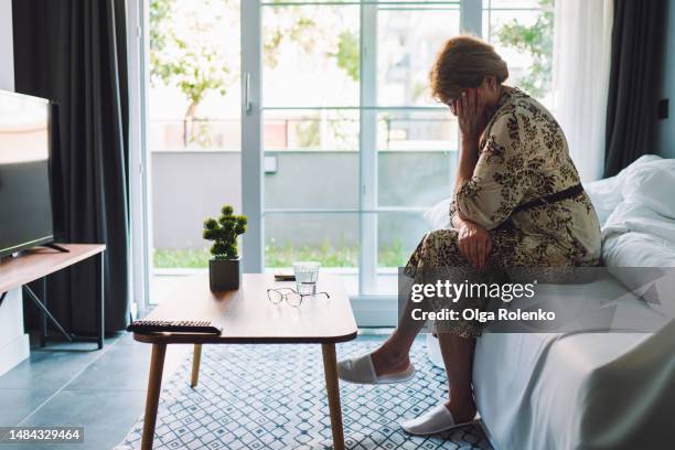 anxiety and memory loss. senior woman crying with face in hands against bright window in nursing home ward - dementie stockfoto's en -beelden