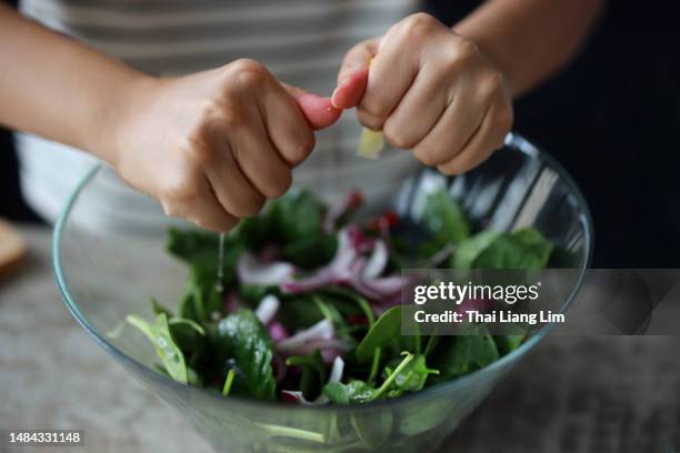 young asian girl squeezing lemon over salad bowl, preparing healthy food at home. - vegan stock pictures, royalty-free photos & images