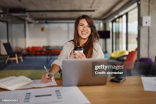 mujer creativa feliz tomando notas mientras trabaja en una computadora portátil en la oficina. - chica-tomando-cafe fotografías e imágenes de stock