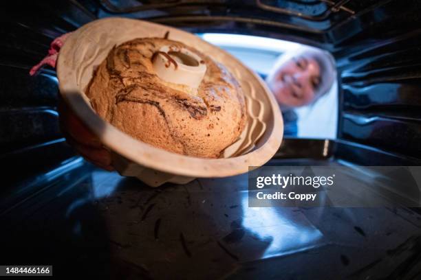 young woman baking kugelhupf in silicone mold and taking it  out of oven - making cake stockfoto's en -beelden