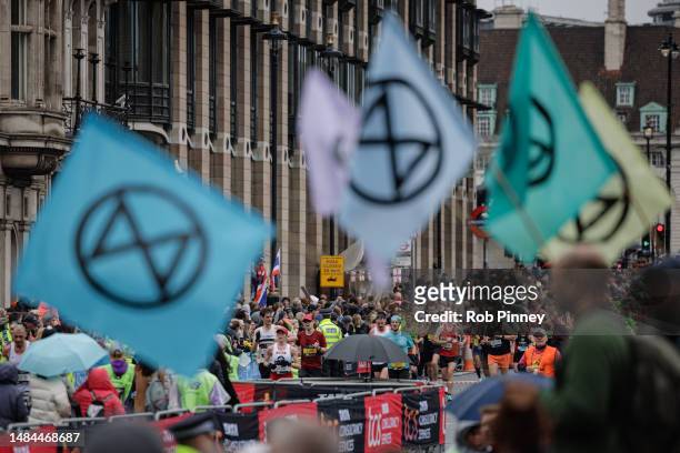 Extinction Rebellion protesters wave flags as London Marathon runners pass through Parliament Square on April 23, 2023 in London, England. XR and...