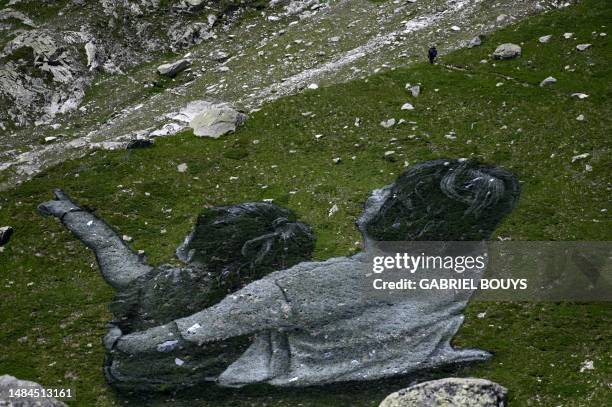 Man walks by French Land artist Guillaume Legros aka "Saype" new giant land art fresco entitled: "La Grande Dame" in Courmayeur, on July 3, 2023. The...