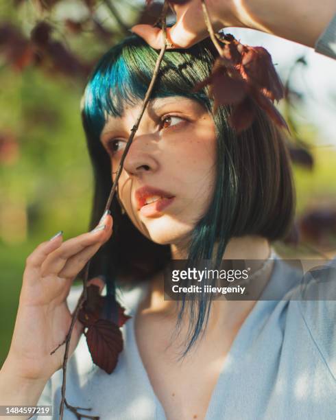 asian woman with dyed blue hair on background of spring tree. bang hairstyle. garden. white flowers - gothic style stockfoto's en -beelden