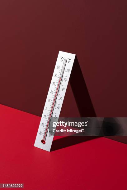 silver thermometer shows high temperature on red background - thermometer stockfoto's en -beelden