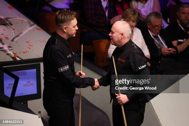 John Higgins of Scotland shakes hands with Kyren Wilson of England following their round two match on Day Nine of the Cazoo World Snooker...