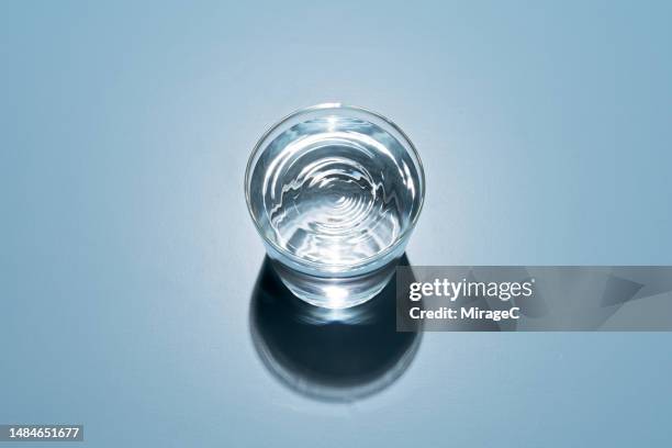 water in a glass cup on blue background - agua purificada fotografías e imágenes de stock