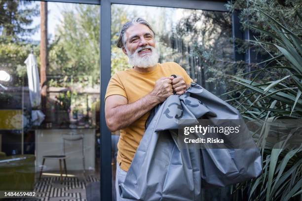 adult man carrying two trash bags full of waste to recycle - white garbage bag stock pictures, royalty-free photos & images