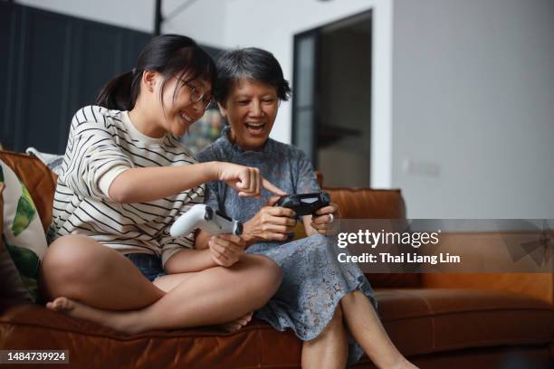 a cheerful asian grandmother and his granddaughter are sitting on the sofa in the living room, learning and having fun playing video games together at home. this heartwarming scene embodies the happy retirement concept. - chinese girl stock pictures, royalty-free photos & images