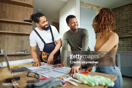 Happy black couple and manual worker working on blueprints at home.