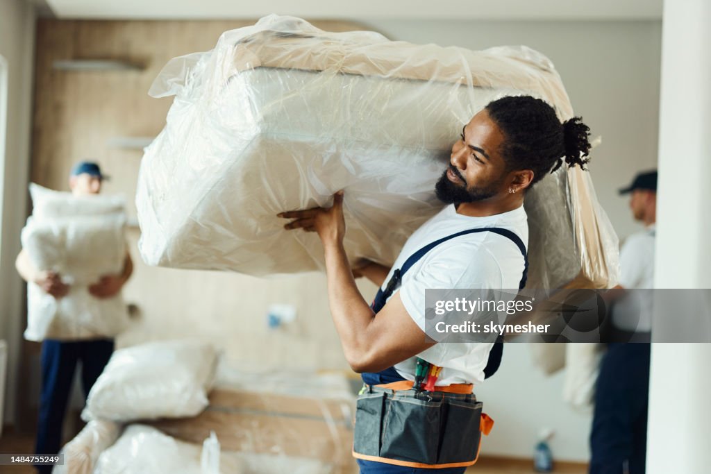 Young black mover carrying furniture in a new apartment.
