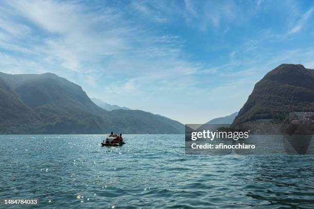 distant rear view of two women sailing in a paddle boat, lake lugano, switzerland - tretboot stock-fotos und bilder