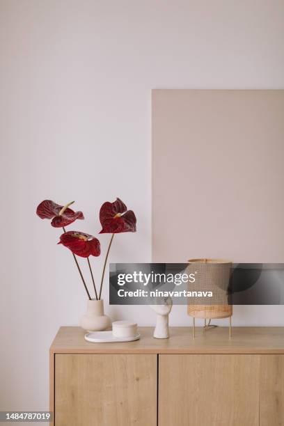 vase with anthurium flowers and ornaments on a wooden sideboard with blank artwork on the wall - anthurium stock pictures, royalty-free photos & images