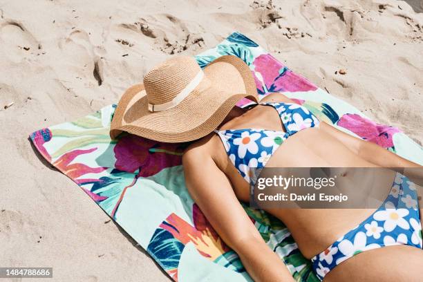 unrecognizable woman lying on a beach towel with her face covered by a beach hat - sunbathing stock pictures, royalty-free photos & images