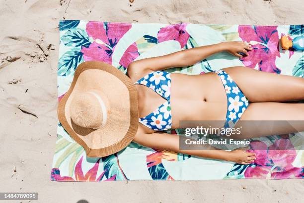 top view of an unrecognizable woman lying on a beach towel with her face covered by a beach hat - woman towel beach stockfoto's en -beelden