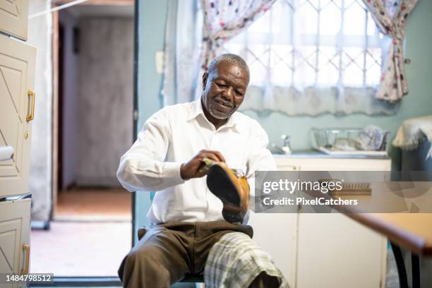 heureux senior bien habillé homme africain polissant des chaussures en cuir dans la cuisine - south african culture photos et images de collection