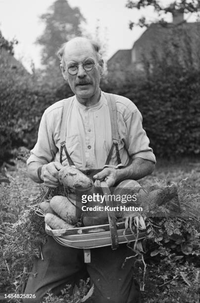 Man holding a trug filled with root vegetables in a garden in Aldworth, Berkshire, March 1945. Original Publication: Picture Post - 1713 - Anne...