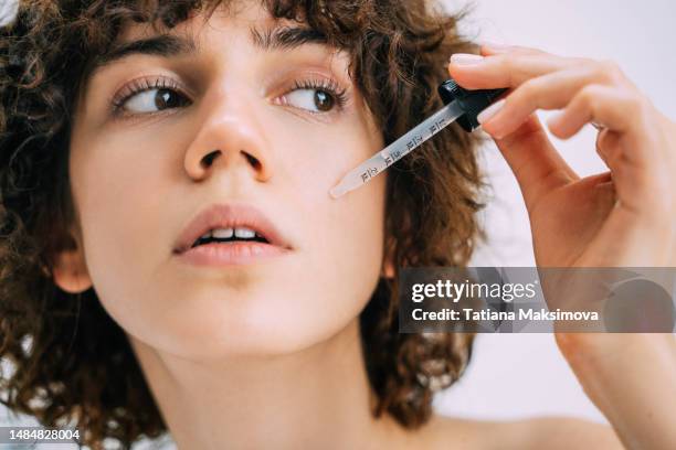 a beautiful young woman applies serum to her face with a pipette. close-up portrait. - retinol stock pictures, royalty-free photos & images
