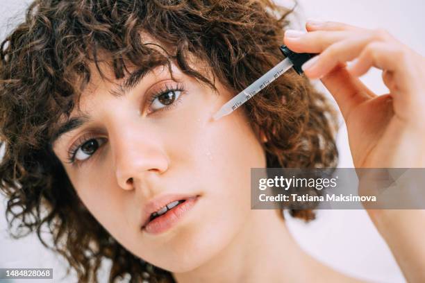 a beautiful young woman applies serum to her face with a pipette. close-up portrait. - complexion foto e immagini stock