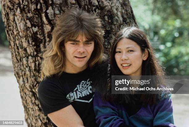 American rock singer Rick Sanford, wearing a t-shirt with the logo of his band 'Legs Diamond', beside an Asia woman, with a tree trunk in the...