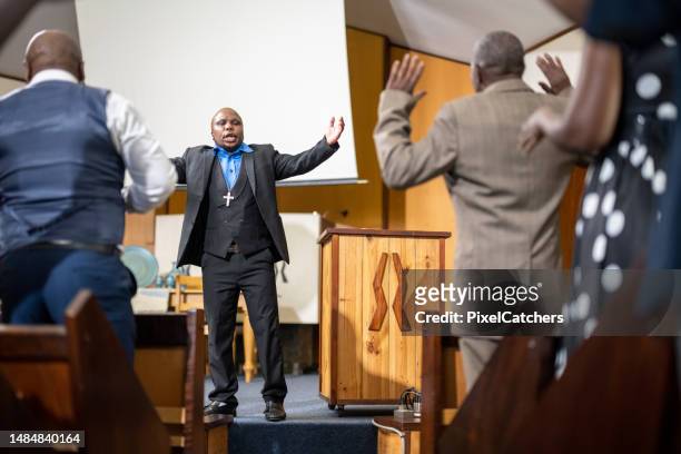 pastor stand preaching with arms raised in front of congregation - gemeenteraad stockfoto's en -beelden