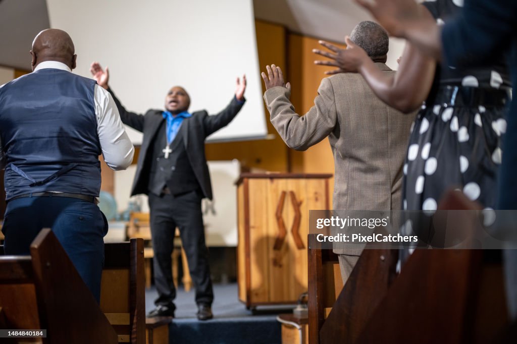 Pastor stand preaching with arms raised in front of congregation