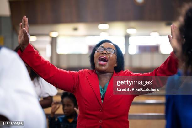 woman in red jacket singing with arms outstretched in church - gospel singer stock pictures, royalty-free photos & images