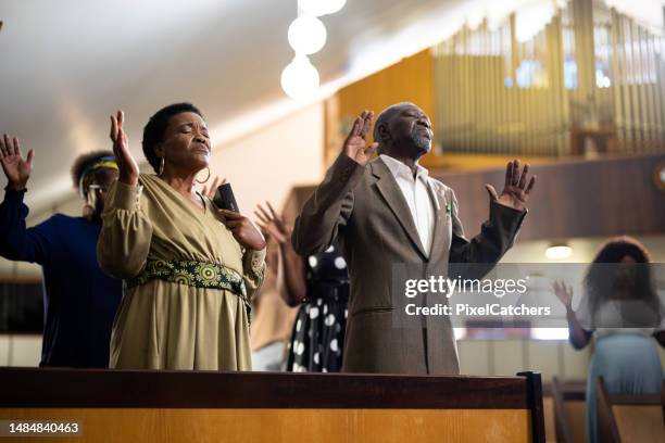 seniors with hands raised standing praying in church - praising religion stock pictures, royalty-free photos & images