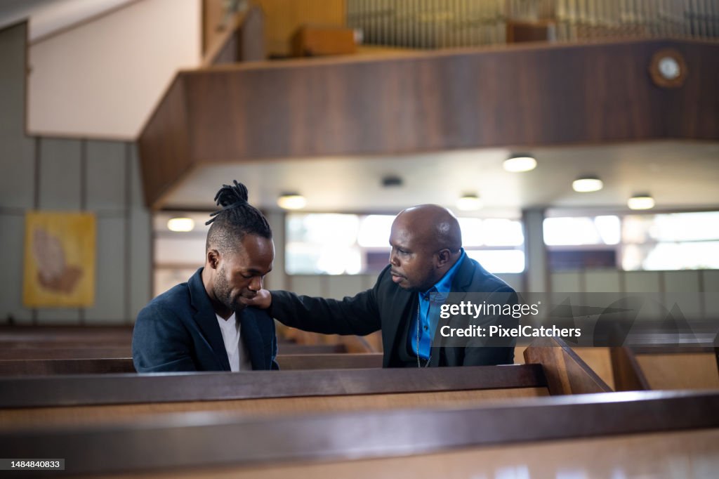 Pastor prays with man sitting in pew in church