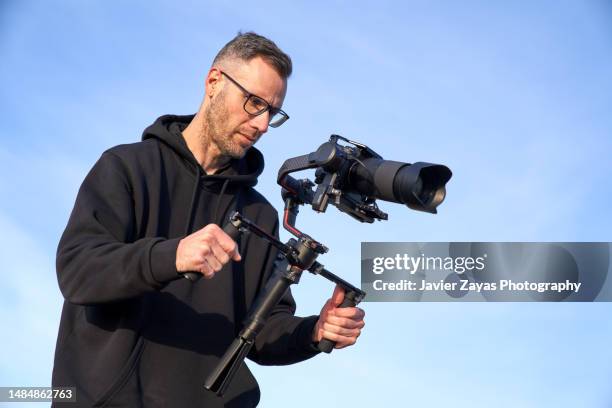 camera operator filming on the beach using a stabilizer - reportage foto e immagini stock
