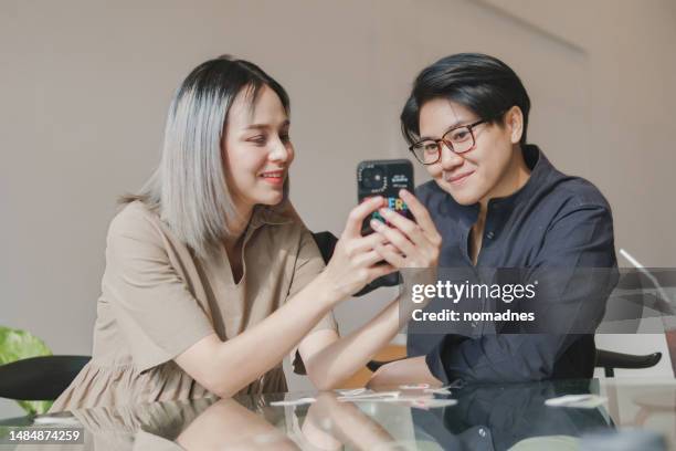 lesbian couple put hands together show the rainbow lgbtqia symbol and using smartphone capturing photo. rainbow flag tattoo on lgbtqia person. female couple enjoying time with lgbtqia love symbol tattoo. - put together stock pictures, royalty-free photos & images