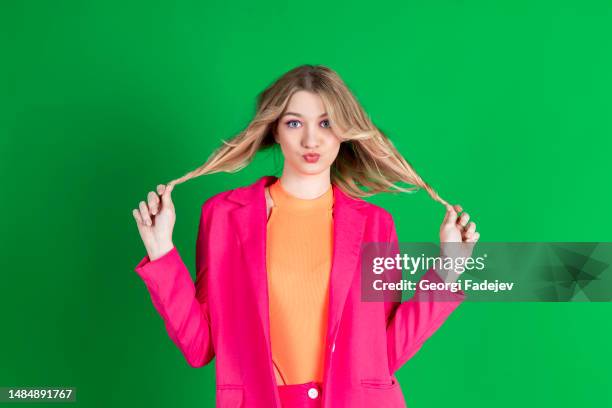 young curly blonde dressed in pink blazer, looking away and holding, pulling her hair to the sides. isolated on green background. - child pulling hair stock pictures, royalty-free photos & images