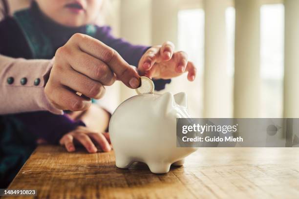 mother and her little daughter puting in savings into a white piggy bank. - bank account stock pictures, royalty-free photos & images