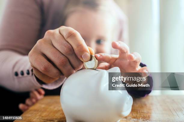 mother and her little daughter puting in savings into a white piggy bank. - blonde girl piggy bank stock-fotos und bilder